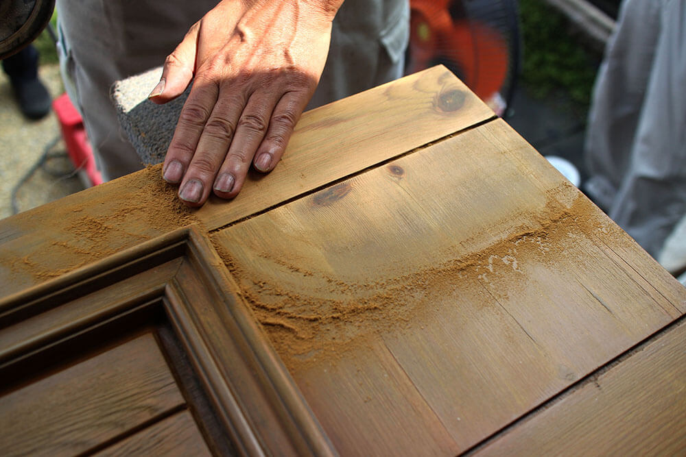 木製玄関ドアを丸サンダーで研磨し、木目がよみがえった部分を確認する職人の手元