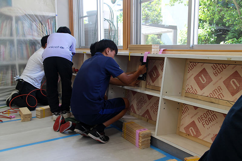 図書室の壁に断熱材とヒノキ板を取り付ける子どもたち
